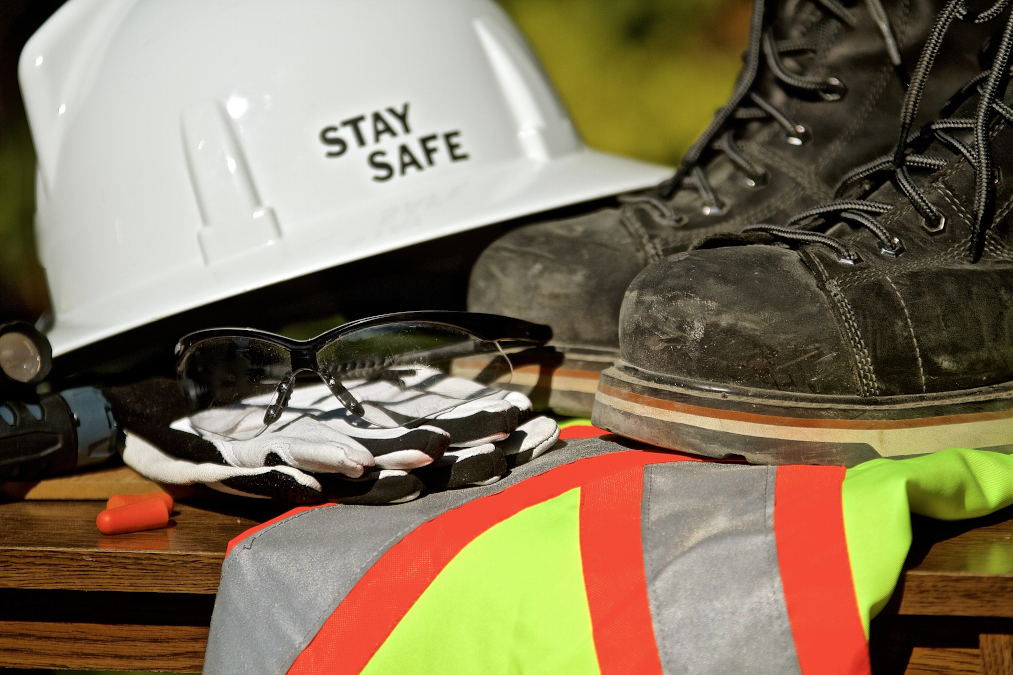 A picture of safety personal protection equipment with a helmet, work boots, safety glasses, vest, and gloves.